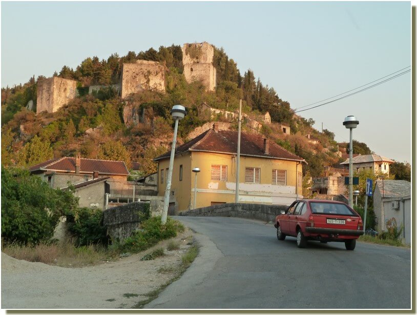 Route traversant Stolac : vue d'une maison et du château en ruines