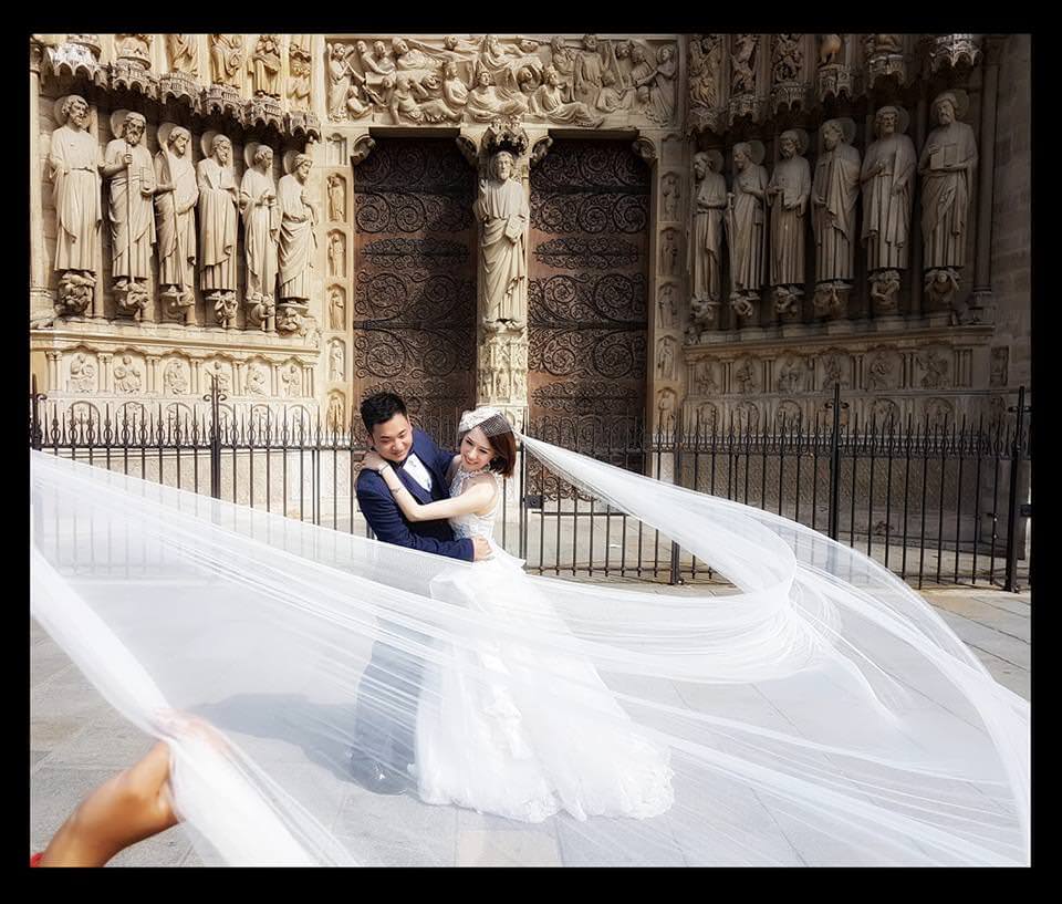 Séance photos de mariage d'un couple chinois assistante tenant le voile devant Notre Dame de Paris