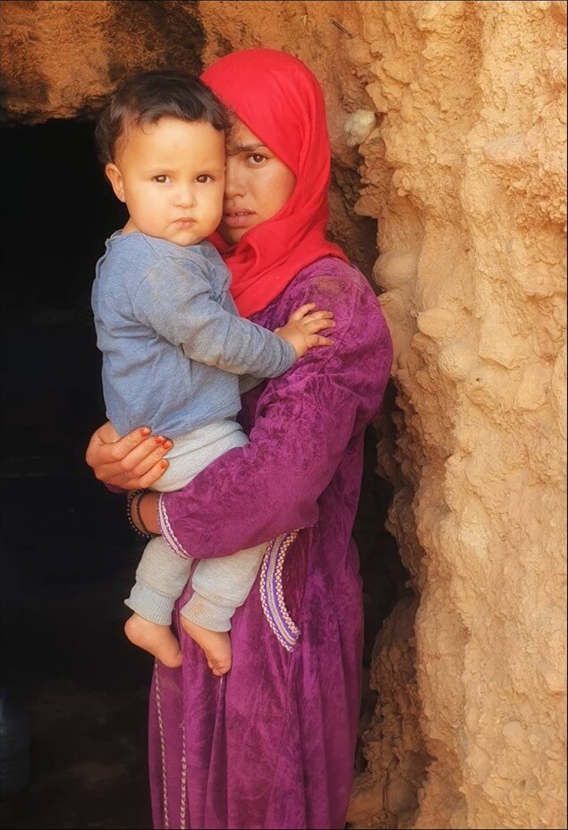 fillette tenant un enfant dans ses bras à l'entrée d'une grotte dans l'atlas marocain 