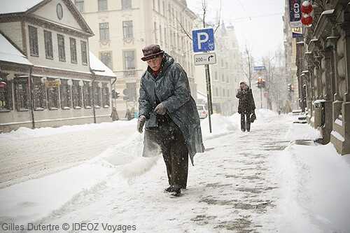 babouchka en train de saler le trottoir alors quil neige a riga