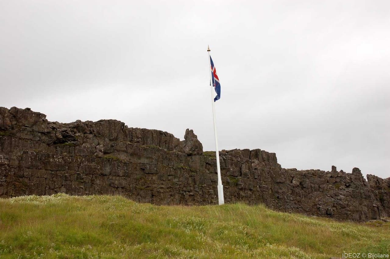 le drapeau islandais flotte sur le lieu du Parlement avec derrière, le Rocher de la Loi.
