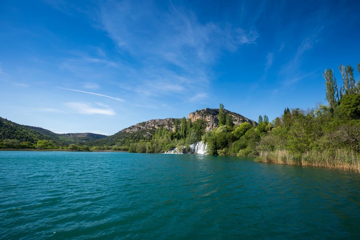 Vue depuis l’eau sur la grande cascade de Roški slap et les rives boisées de la Krka