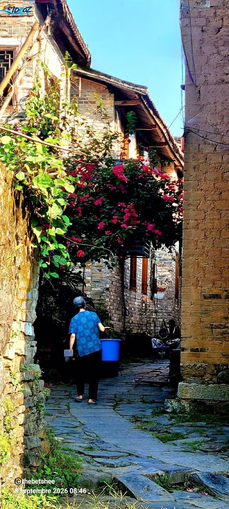 Habitante marchant dans une ruelle pavée du village ancien de Huangyao, entre maisons traditionnelles et bougainvilliers